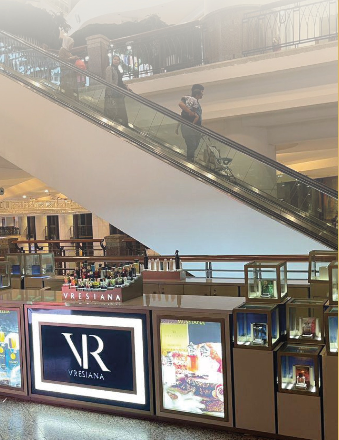 A Vresiana kiosk with glass display cases below a mall escalator
